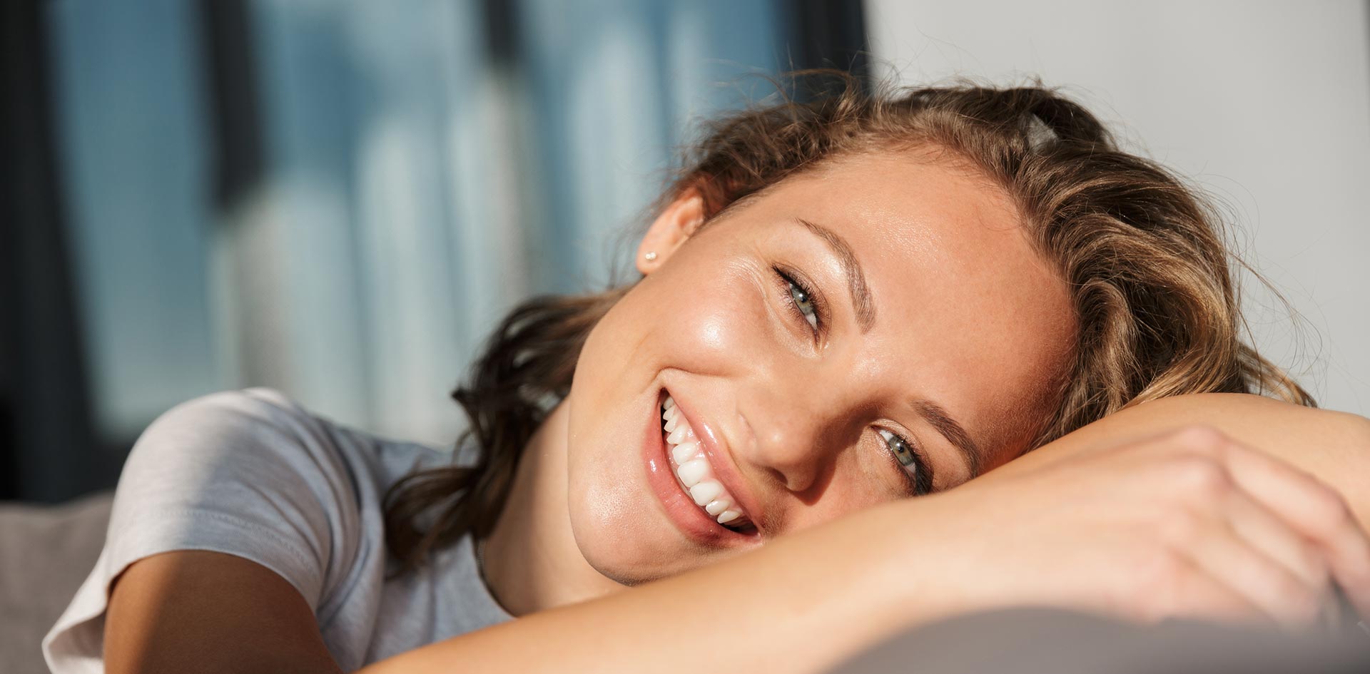 A young woman with blonde hair smiling and resting her head on her hand while lying down.