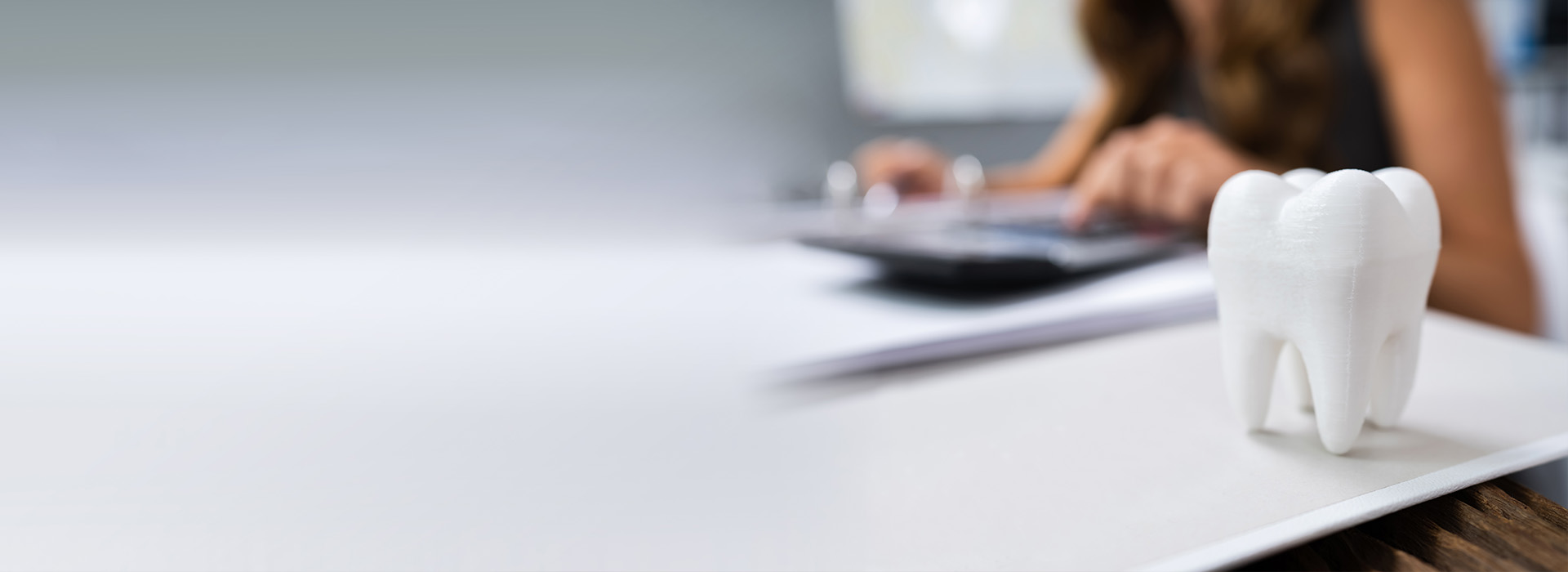 The image shows a person sitting at a desk with a computer monitor, and there s a small figurine of a tooth on the desk.