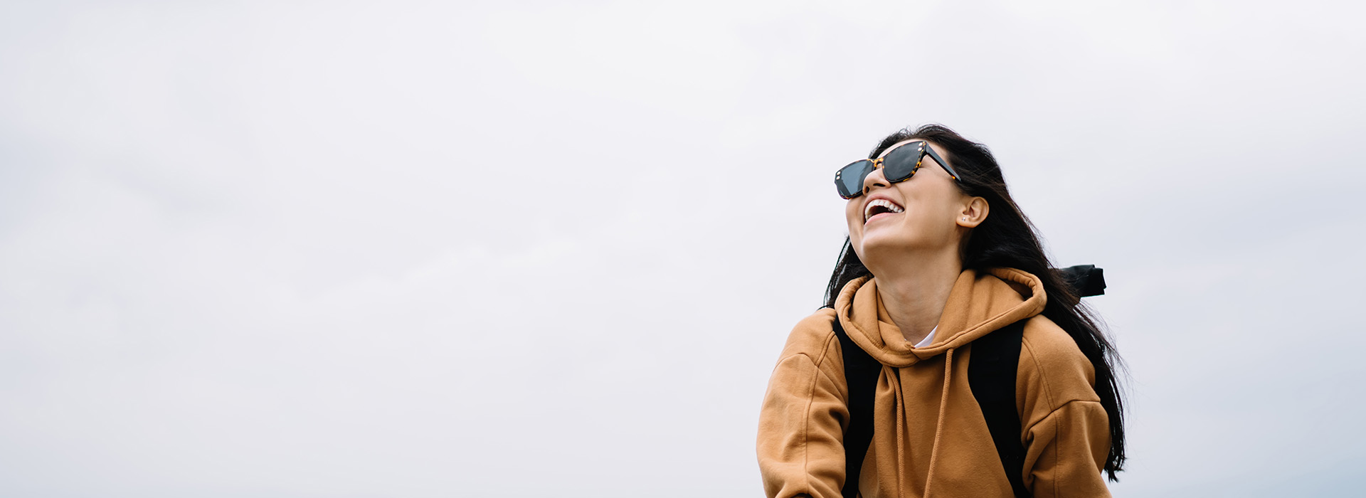 The image shows a person standing on a beach with their back to the camera, wearing sunglasses and a backpack, looking out towards the ocean under a clear sky.
