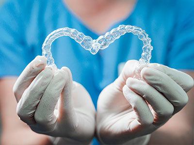 An individual s hand holding a heart-shaped transparent dental retainer against a blue background.