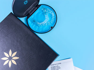 The image shows a pair of opened cosmetic packages with their contents partially visible, placed on a blue surface next to a closed package with a star-shaped design on its lid, and a small blue object that appears to be a product sample.