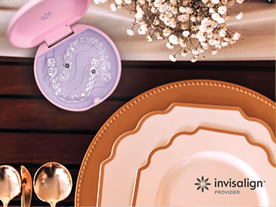 The image shows a dining table set with plates, cutlery, and a decorative item resembling a small pink container with a face design on it. There s a watermark at the bottom right corner that reads  Invisalign   provider.