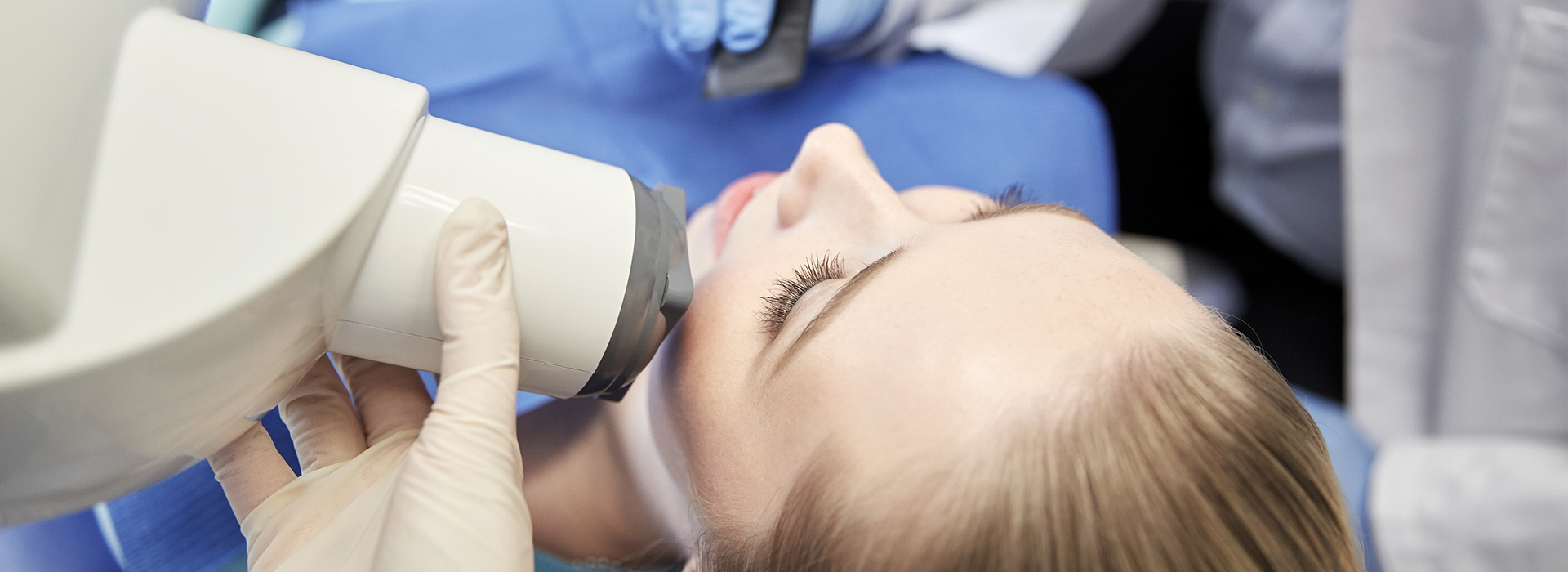 A woman receiving a dental procedure under the supervision of a dentist wearing a protective face mask.