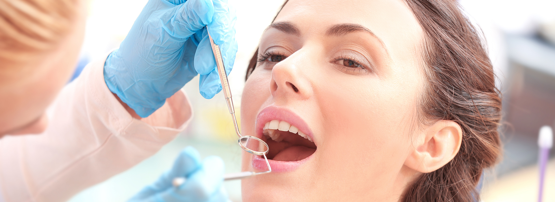 The image shows a woman receiving dental treatment with a syringe while wearing a blue surgical mask, surrounded by other medical personnel.