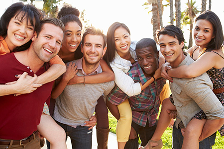 The image shows a group of young adults posing together outdoors, with some holding each other, smiling and appearing happy.
